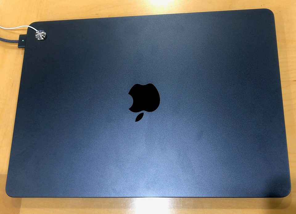 a midnight macbook air with its lid closed on a wooden table, magsafe cable attached