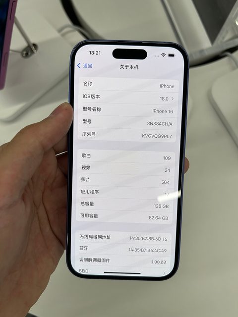 a hand holding an ultramarine iphone 16 showing its about screen