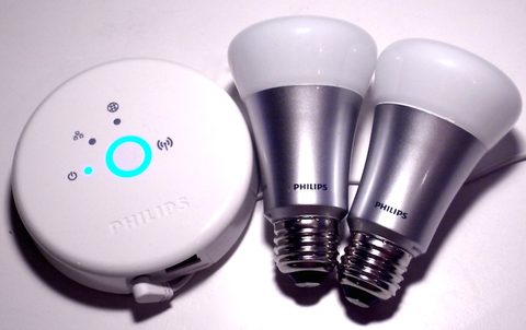 a philips hue bridge hub sitting next to two hue color bulbs
