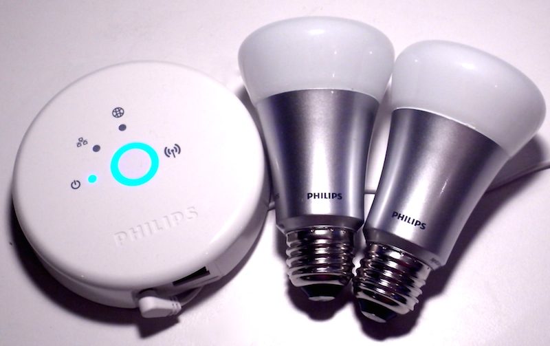 a philips hue bridge hub sitting next to two hue color bulbs