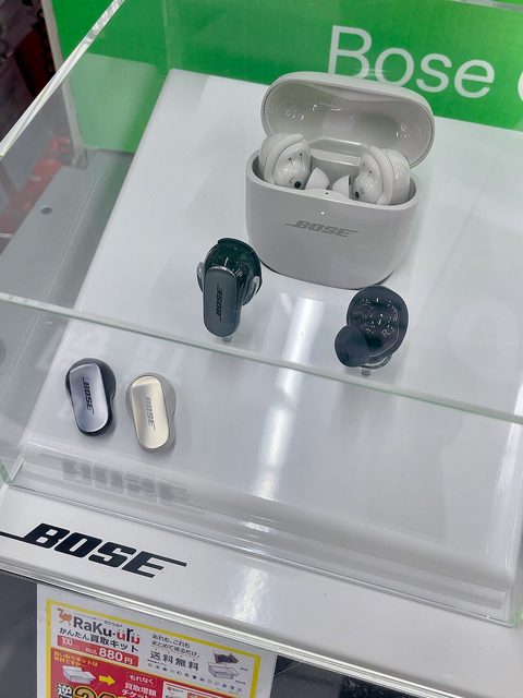 Bose QuietComfort Ultra earbuds and their charging case on a plain surface