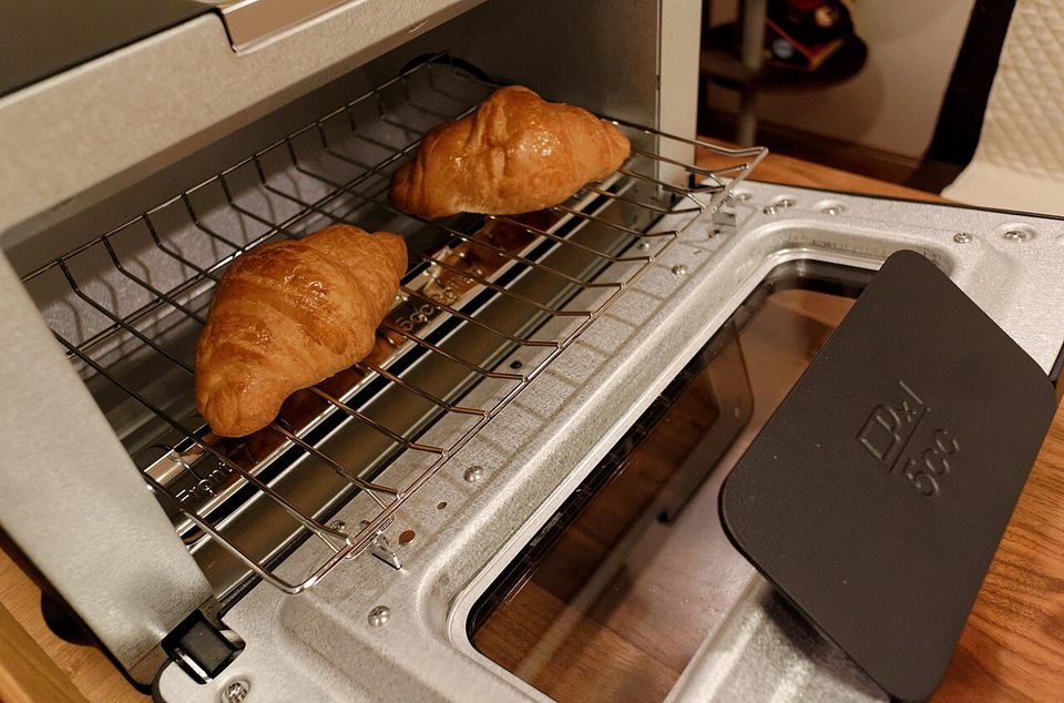 The Balmuda steam toaster, a slim black toaster oven with a small handle, sitting on a counter