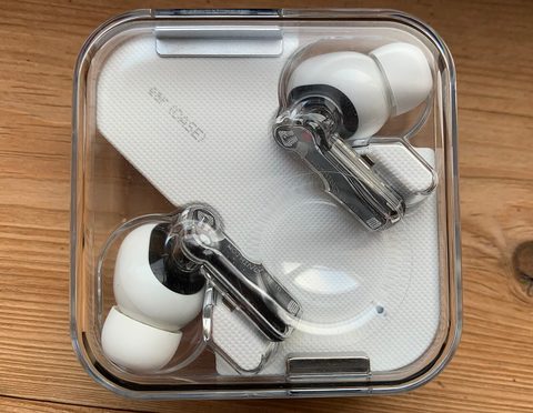 Nothing ear (1) white earbuds in their open transparent charging case on a wooden table