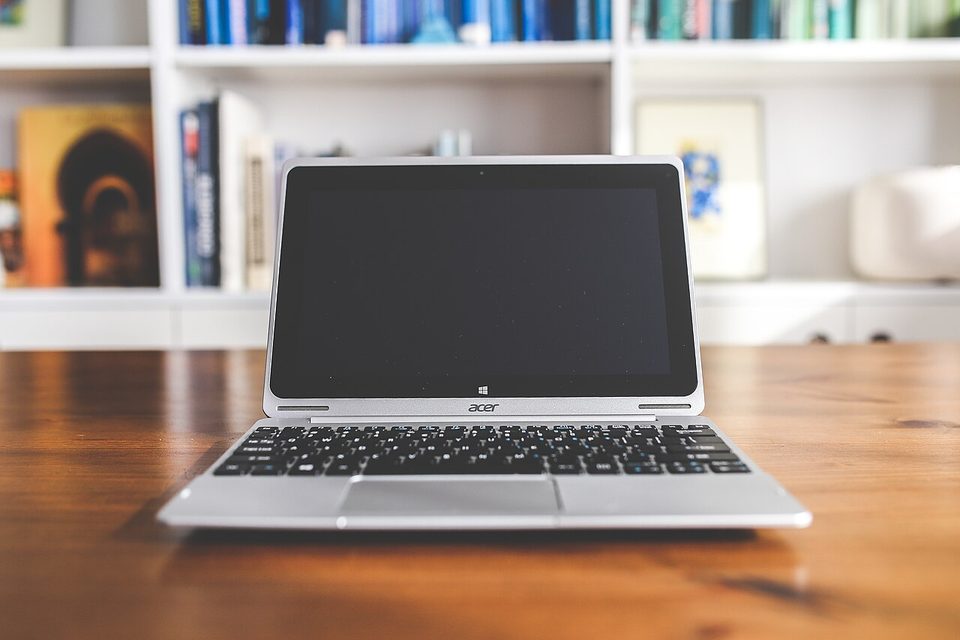 a small silver laptop on a wooden table in front of bookshelves