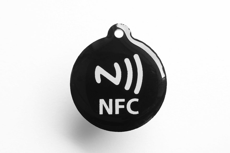 a round black nfc tag printed with the nfc symbol on a white background, the same kind of chip the brick hides inside its little plastic square, not the brick itself