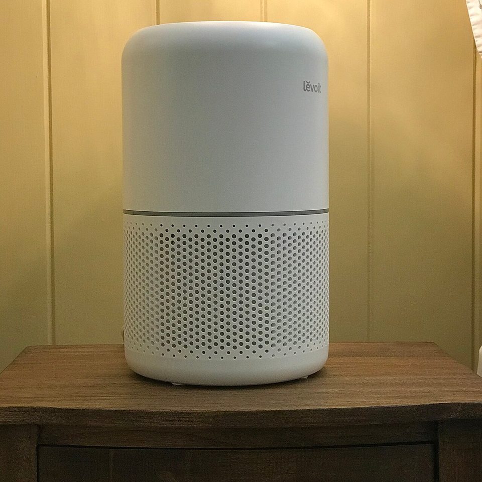 a white levoit core 300 air purifier, the smaller sibling of the core 400s, on a wood nightstand in warm lamplight
