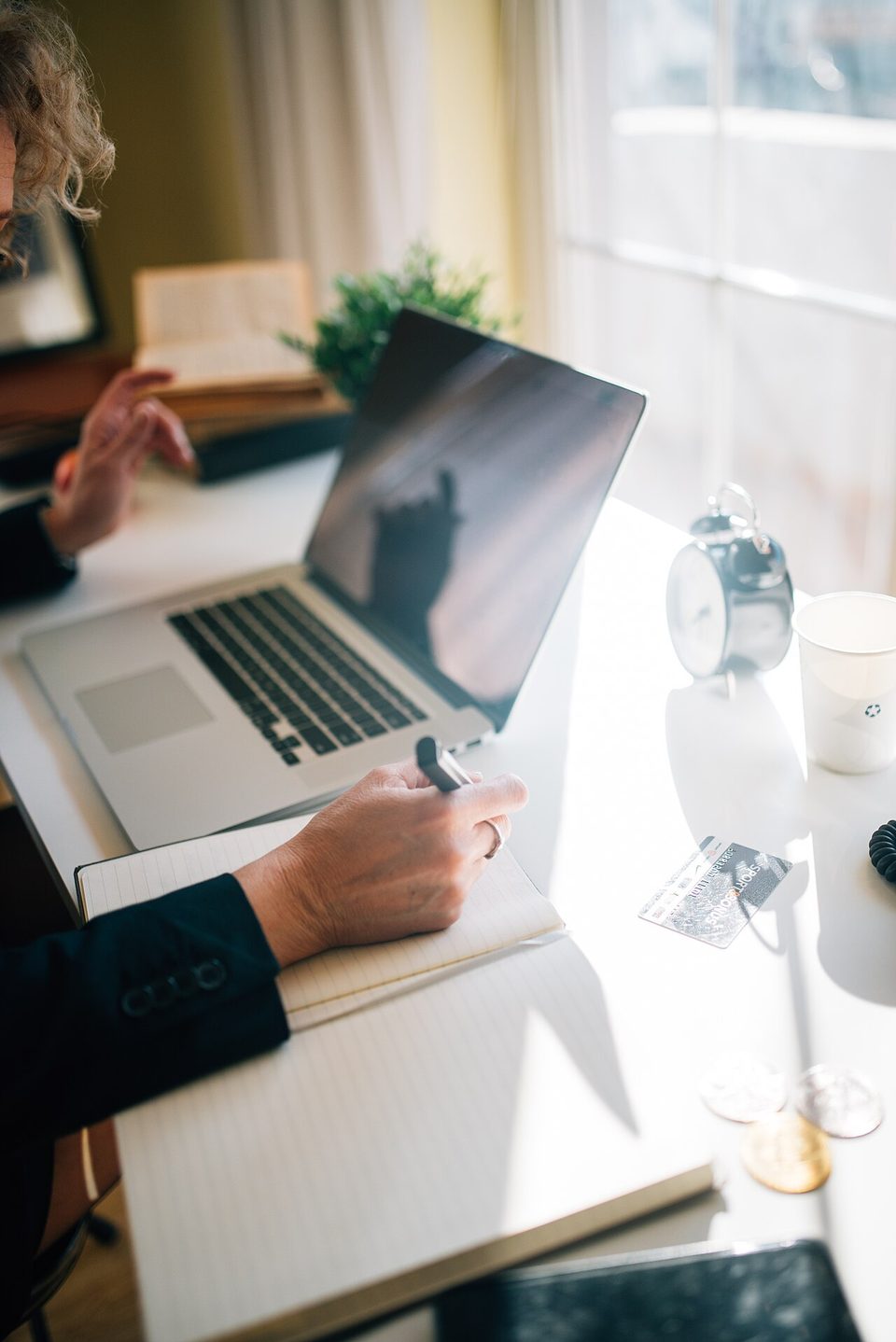 A person writing notes at a desk beside an open laptop