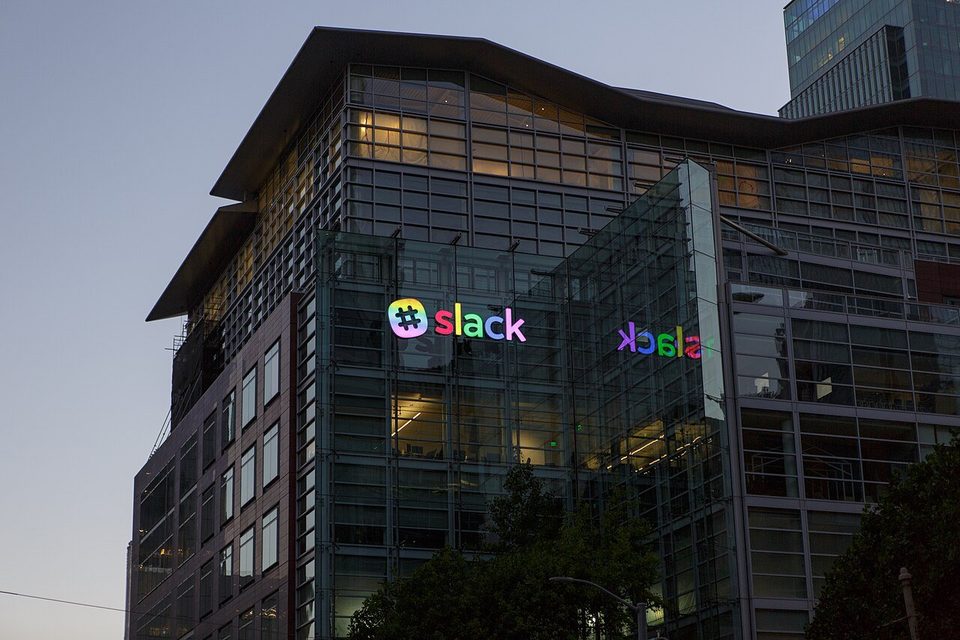 Slack headquarters at 500 Howard Street in San Francisco at dusk, with the lit Slack logo on the glass facade