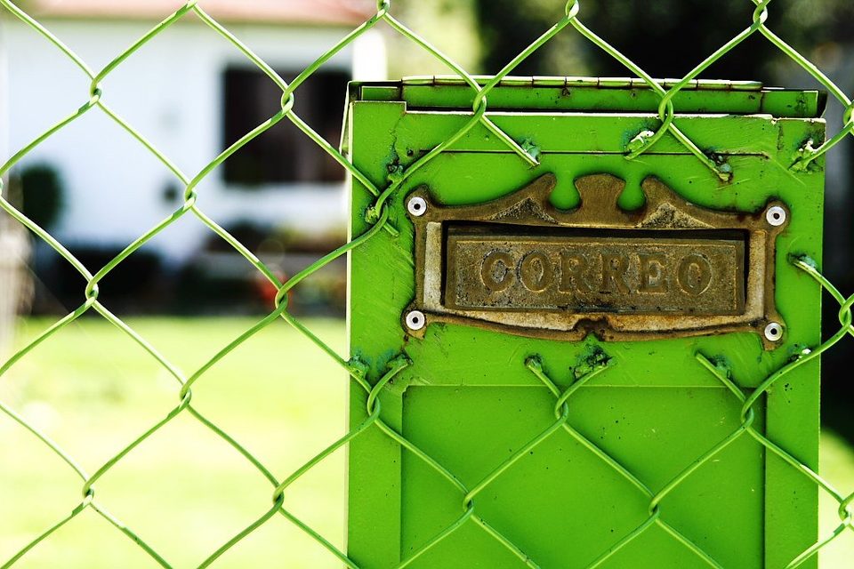 A green letterbox marked Correo mounted behind a chain-link fence