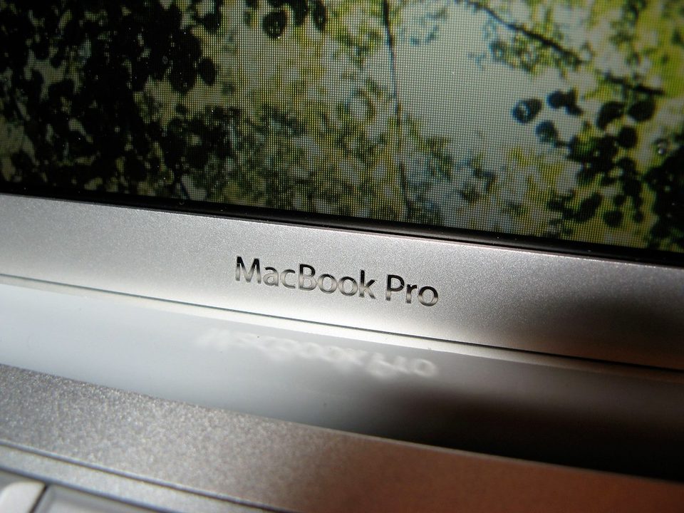 An open MacBook Pro on a desk in a darkened room, the machine most of these essays were written on
