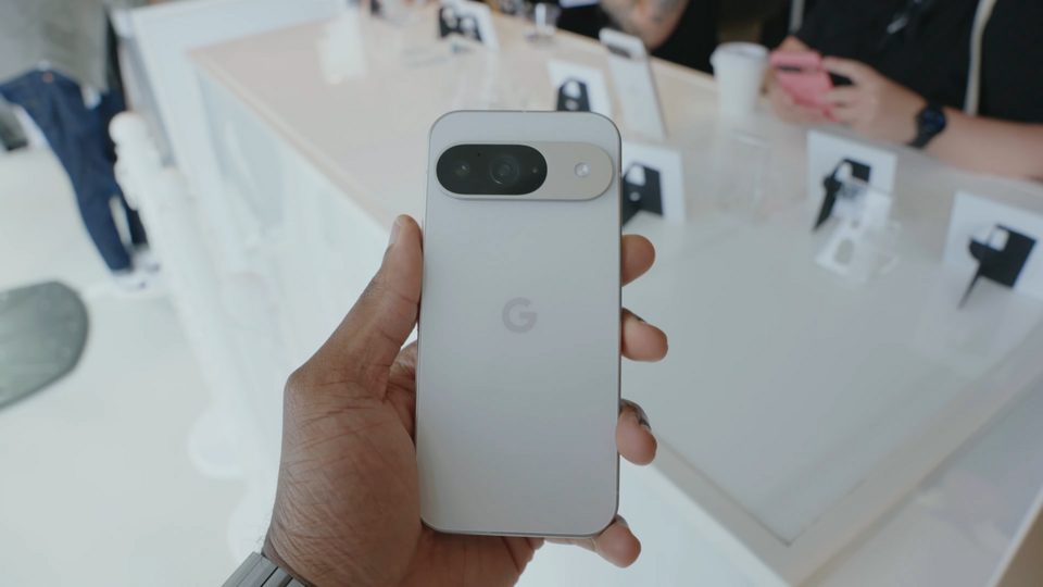 A hand holding the back of a porcelain Pixel 9 Pro at a Google launch event, camera bar and all