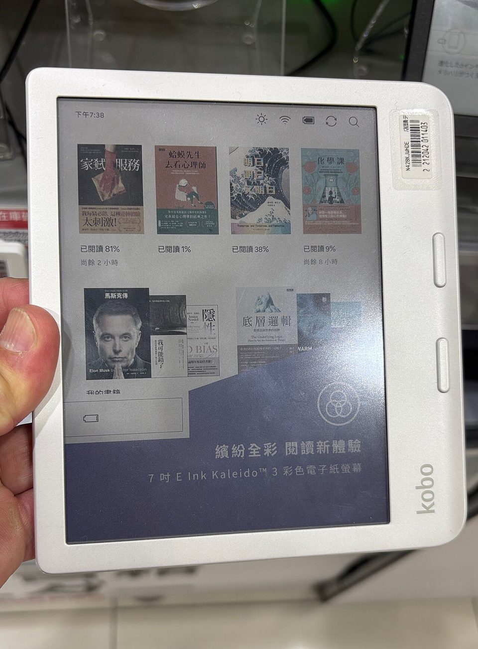 A white Kobo Libra Colour in hand, a grid of book covers on its color E Ink screen and the two page-turn buttons on the wide bezel
