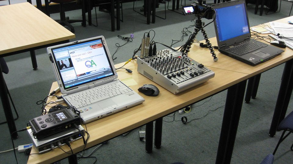 A laptop, headset and microphone arranged on a desk as a teaching rig for a live online course
