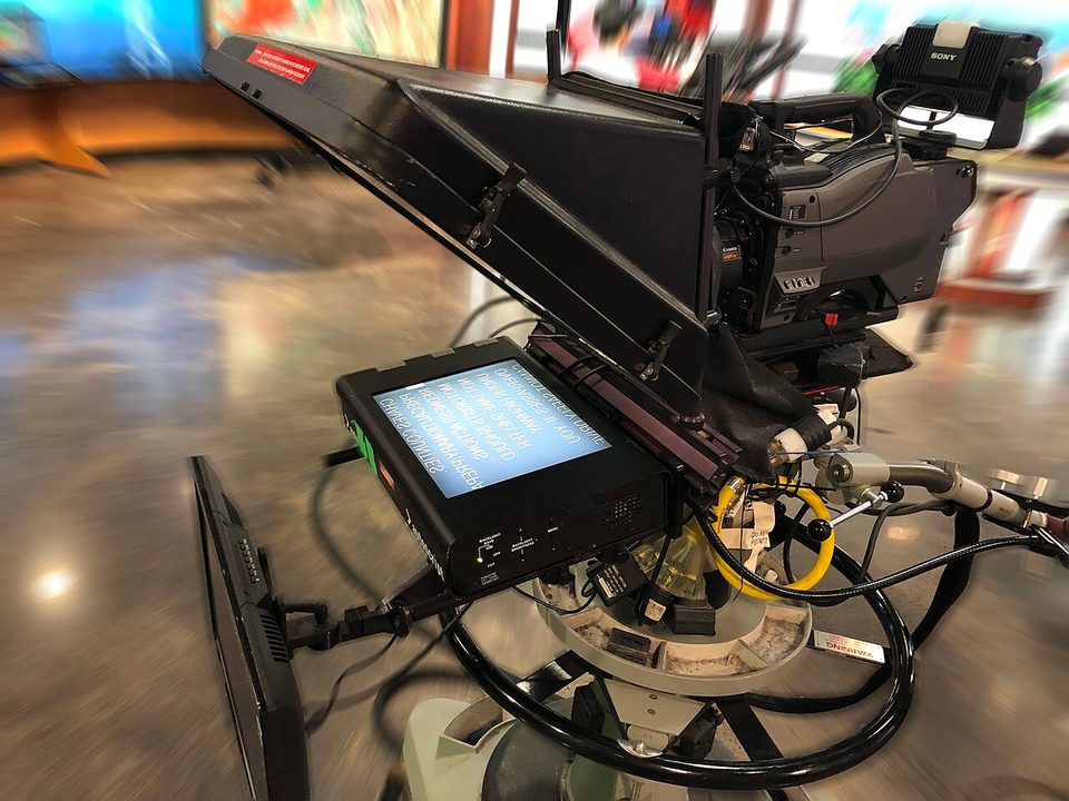 A studio teleprompter with beam-splitter glass in front of a camera, the arrangement the Prompter miniaturises for a desk