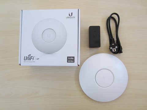 A first-generation UniFi access point beside its box, power adapter and Ethernet cable