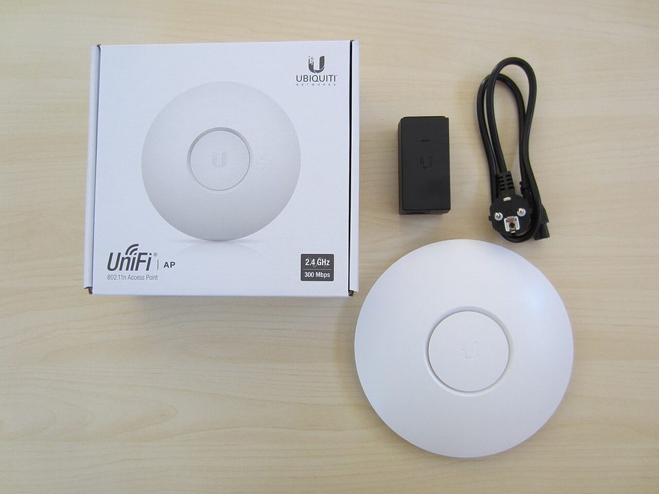 A first-generation UniFi access point beside its box, power adapter and Ethernet cable