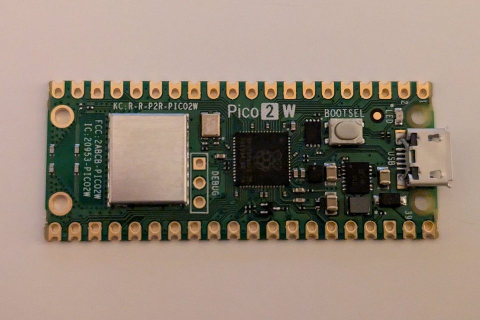 A Raspberry Pi Pico 2 W board seen from above, with its shielded wireless module, RP2350 chip, BOOTSEL button and micro USB port, on a pale surface