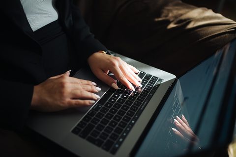 A person typing on a laptop while holding a smartphone with apps open