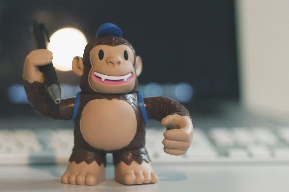 A vinyl toy of Freddie, the Mailchimp chimp mascot, standing in front of a computer keyboard