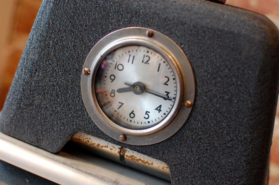 Close-up of an old punch clock's round dial above the slot where time cards go in